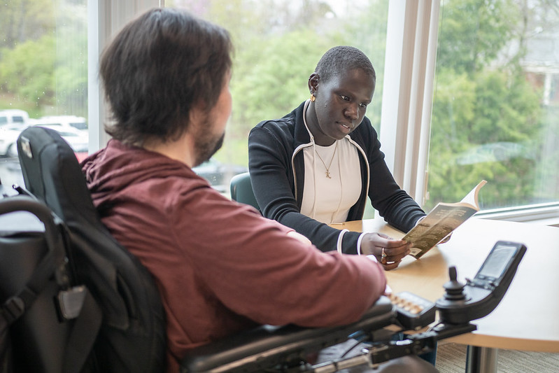 An advisor wearing a black top goes over notes with young student in a power chair wearing a red sweatshirt